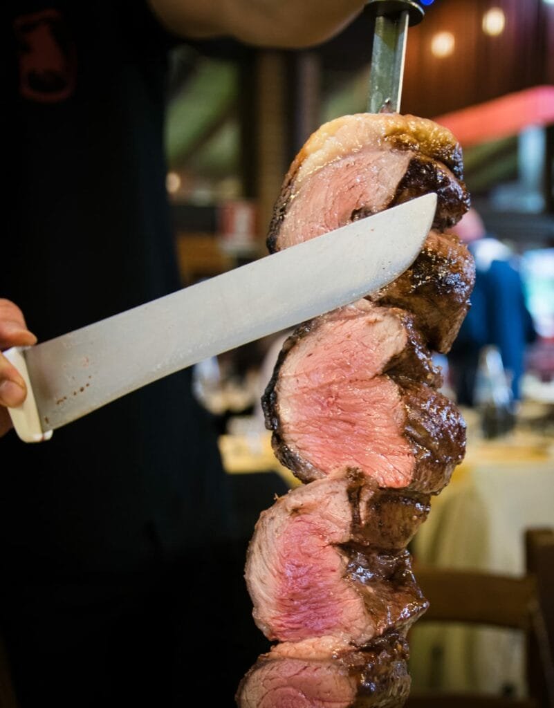 A man cutting a steak with a knife at a Brazilian Steakhouse.